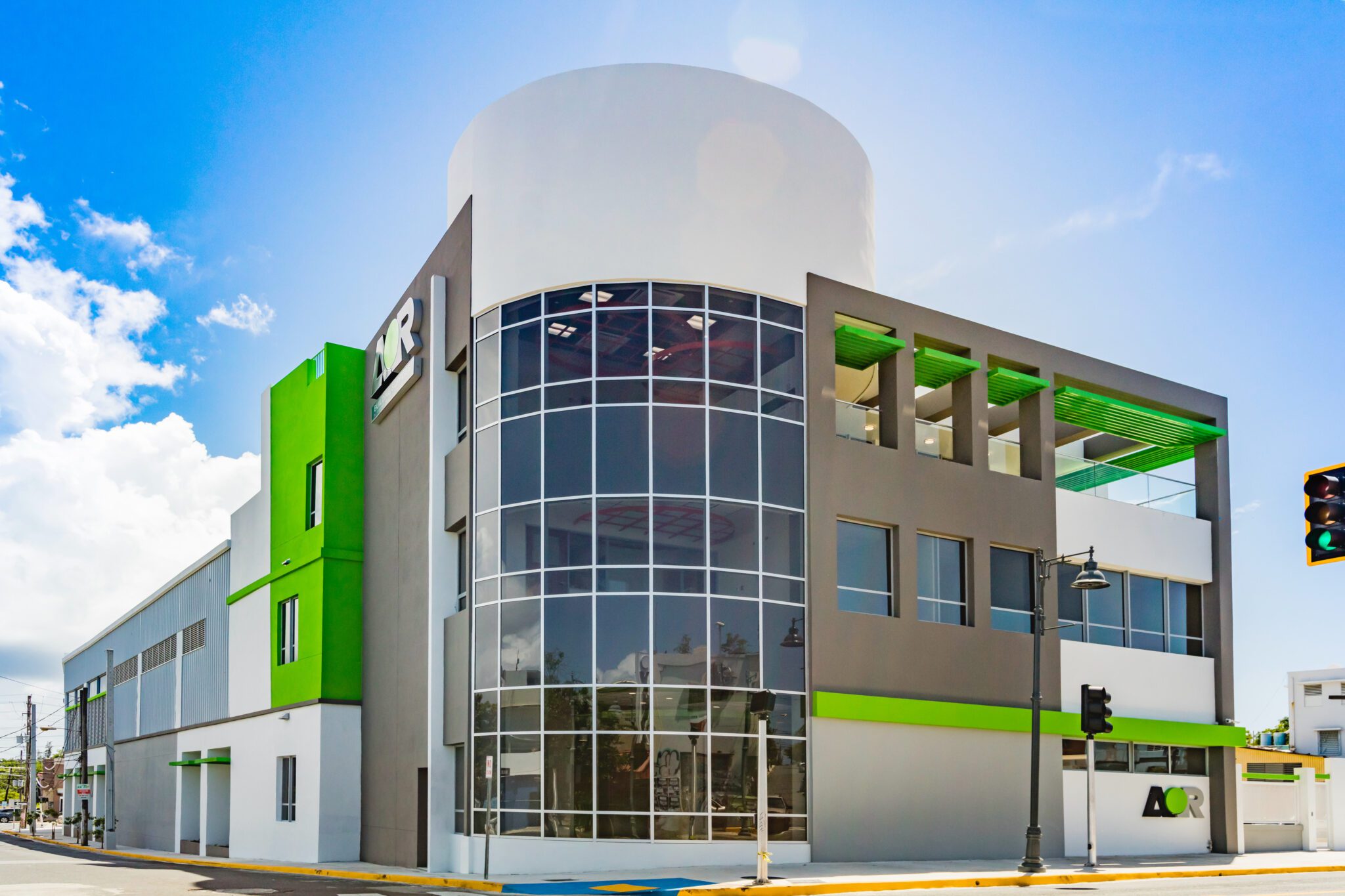 Modern commercial building with glass facade and green accents under a clear blue sky.