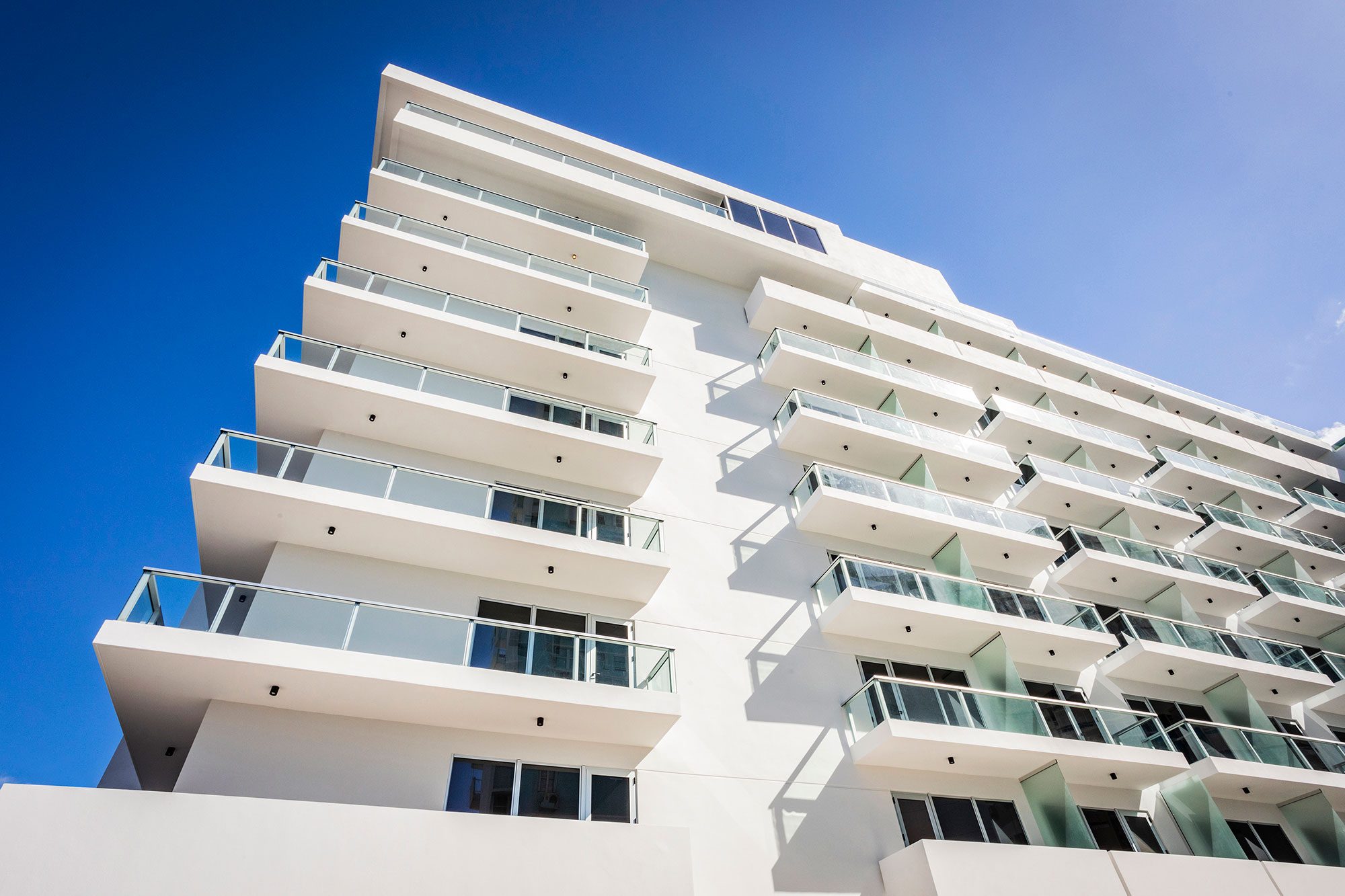 Modern white apartment building with balconies against a clear blue sky.