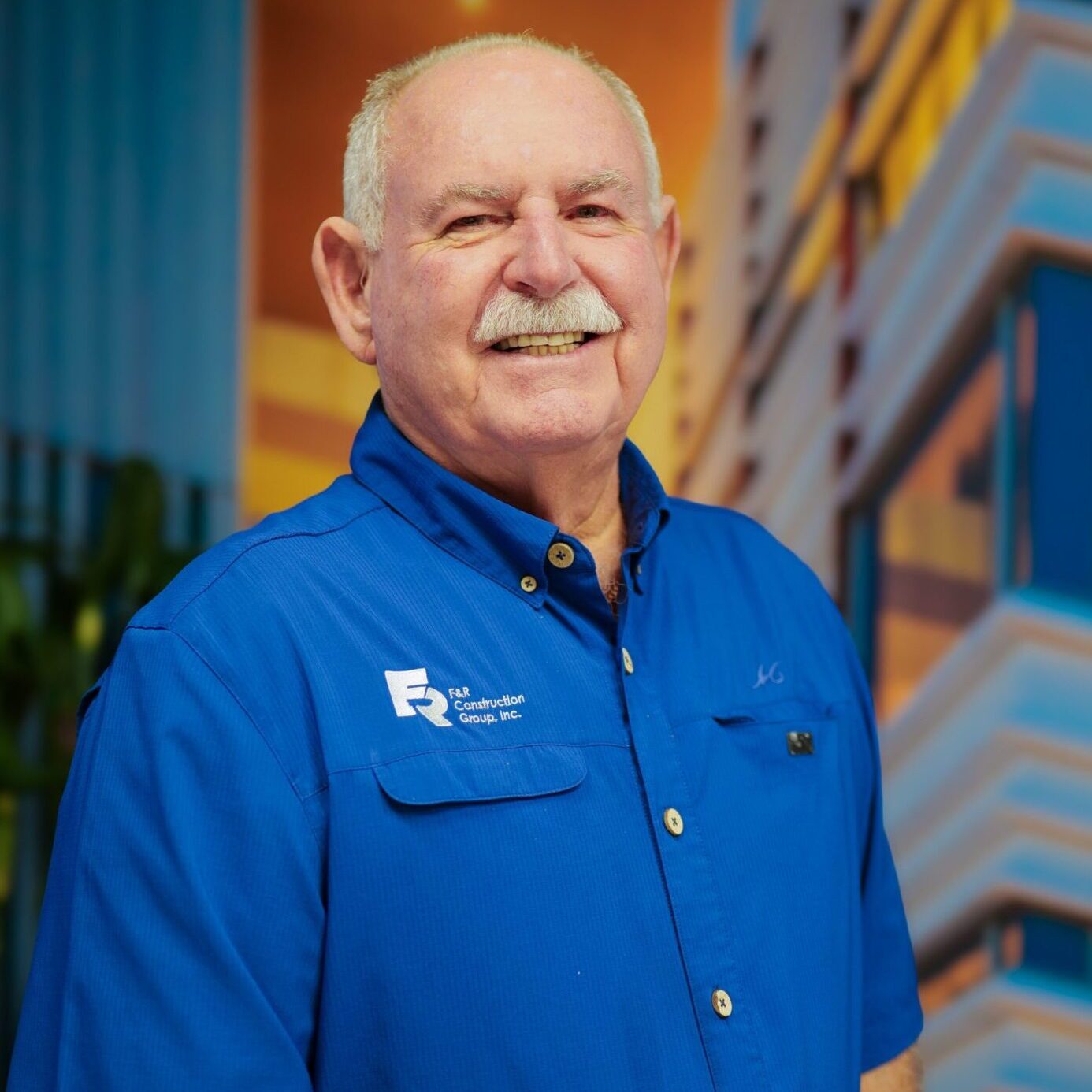 Portrait of a smiling elderly man in a blue shirt with a mustache.
